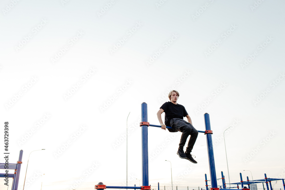 Young man sitting on horizontal bar on sports ground Young man sitting on horizontal bar on sports ground