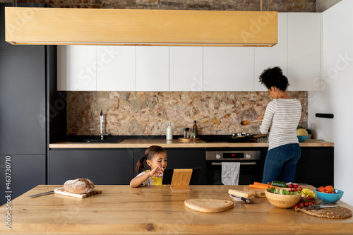 Kid with a tablet and mum cooking at kitchen photo