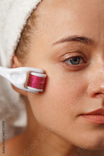 Woman applying derma roller on face photo
