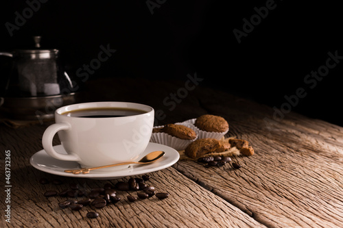 Coffee cup with cookie bread bakery or breakfast cake laying on a wooden table on a black needle background © WIROT