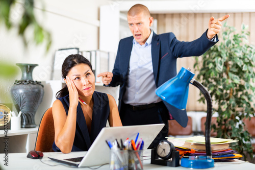 Angry boss criticizing sad frustrated employee sitting at office desk at work