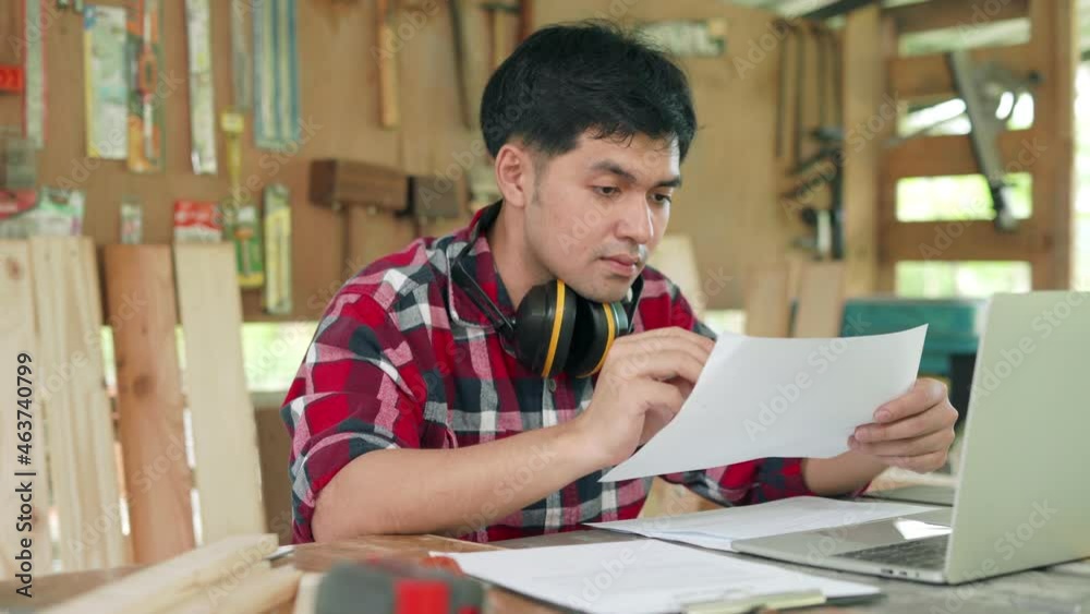 Small business owner carpentry concept. Asian man owns recheck wood furniture. carpenter is Recheck straight of wood before manufacturing. Comparison of material with designs. Small business owner carpentry concept. Asian man owns recheck wood furniture. carpenter is Recheck straight of wood before manufacturing. Comparison of material with designs.