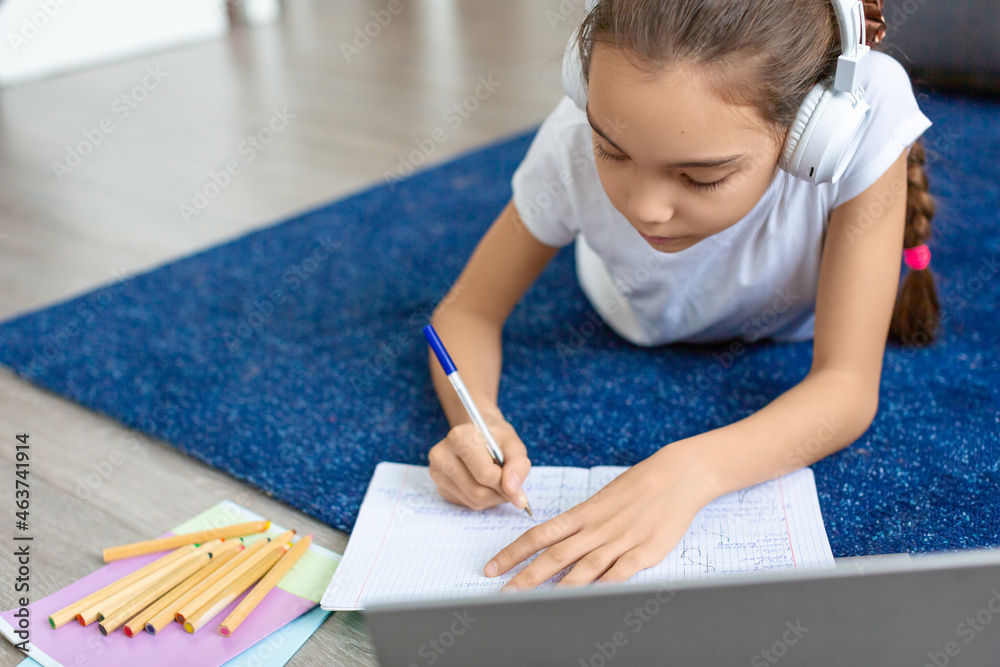 Schoolgirl doing homework online in front of a laptop monitor. She lies on the floor in front of a laptop monitor. Schoolgirl doing homework online in front of a laptop monitor. She lies on the floor in front of a laptop monitor.