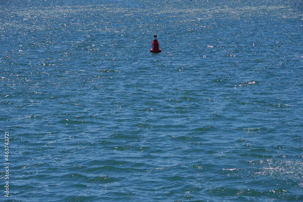 A single large red buoy marke No. 8 floating in the blue ocean water near a harbor entrance