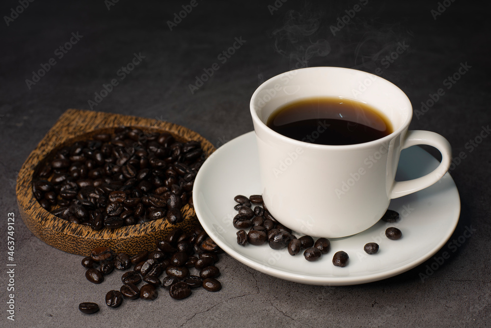 Fototapeta premium A cup of hot black coffee on a black background with roasted coffee beans and hot steam coming out of the mug..