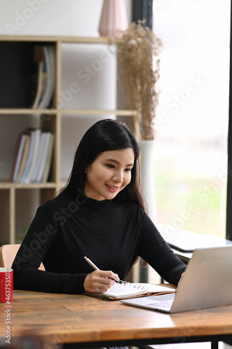 Smiling young woman designer sitting in creative workplace and working with laptop computer.