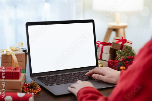 Woman using and typing on Laptop with a mockup white screen and christmas decorations in living room.
