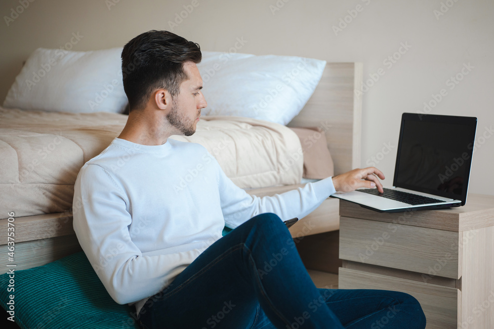 Man sitting on the floor leaning on the bed and typing on the computer. Online career. Internet technology. Sitting man. Computer technology. Business