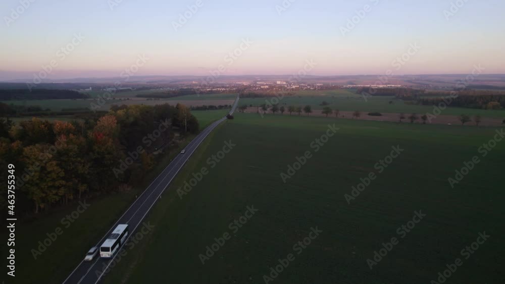 View of passing cars and a bus on the road leading to the city at sunset in autumn View of passing cars and a bus on the road leading to the city at sunset in autumn