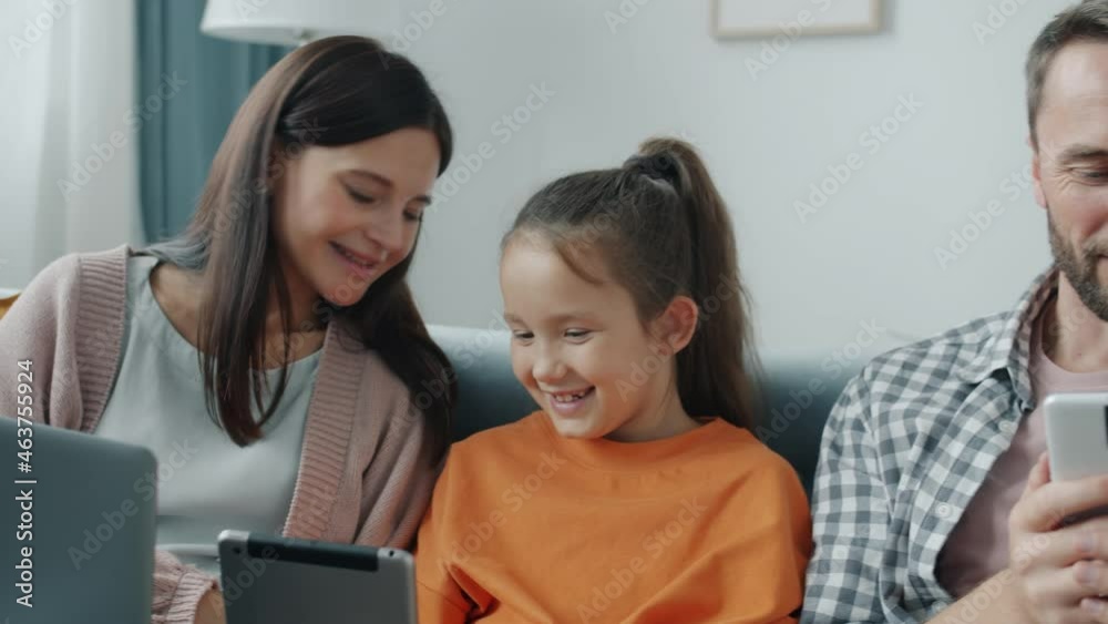 Mother and daughter are enjoying tablet laughing while father is using smartphone texting relaxing on couch at home. Gadgets and lifestyle concept. Mother and daughter are enjoying tablet laughing while father is using smartphone texting relaxing on couch at home. Gadgets and lifestyle concept.