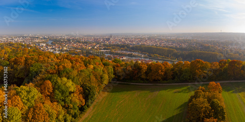 Drone point of view over skyline of Regensburg, Bavaria behind beautiful colorful variegated autumn foliage of deciduous forest on sunny day in October