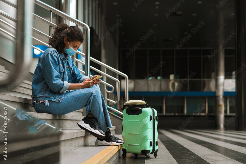 Black woman using cellphone while sitting on stairs at train station