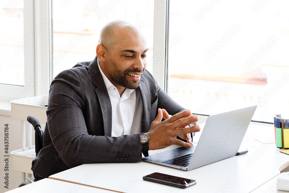 Unshaven man in wheelchair smiling while working with colleagues Unshaven man in wheelchair smiling while working with colleagues
