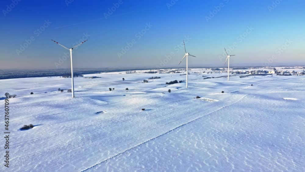 Wind turbines on snowy field in sunny winter day.