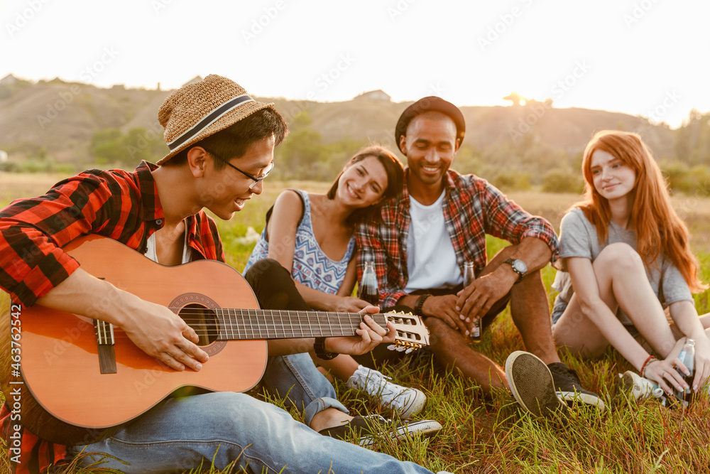 Multiracial friends smiling and playing guitar while sitting on grass