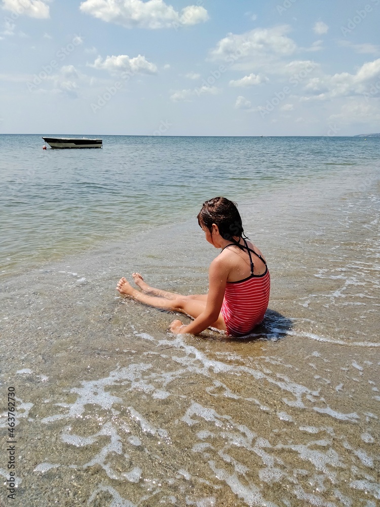 Little girl on the beach sitting in water Stock Photo | Adobe Stock