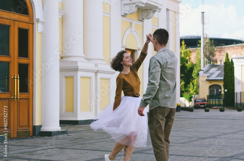 Love story of stylish funny couple: young man in a t-shirt. And a cute young woman in wedding white skirt and yellow sweater. Family holiday and togetherness, date.