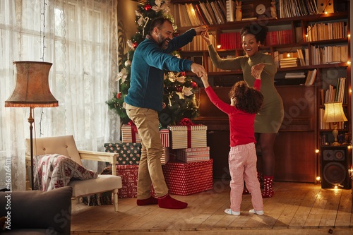 Cheerful family celebrating Christmas at home. They are holding hands, dancing around Christmas tree