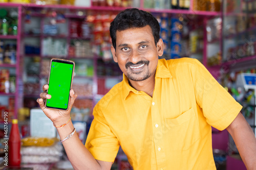 Smiling Merchant at groceries store hold mobile with green screen mock up by looking at camera - concept of Technology, advertisement, online booking and e-commerce photo