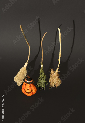 Witch´s broomssticks and Halloween pumpkin lantern standing on black backgroumd. Funny Halloween minimal decoration concept, vertical composition photo