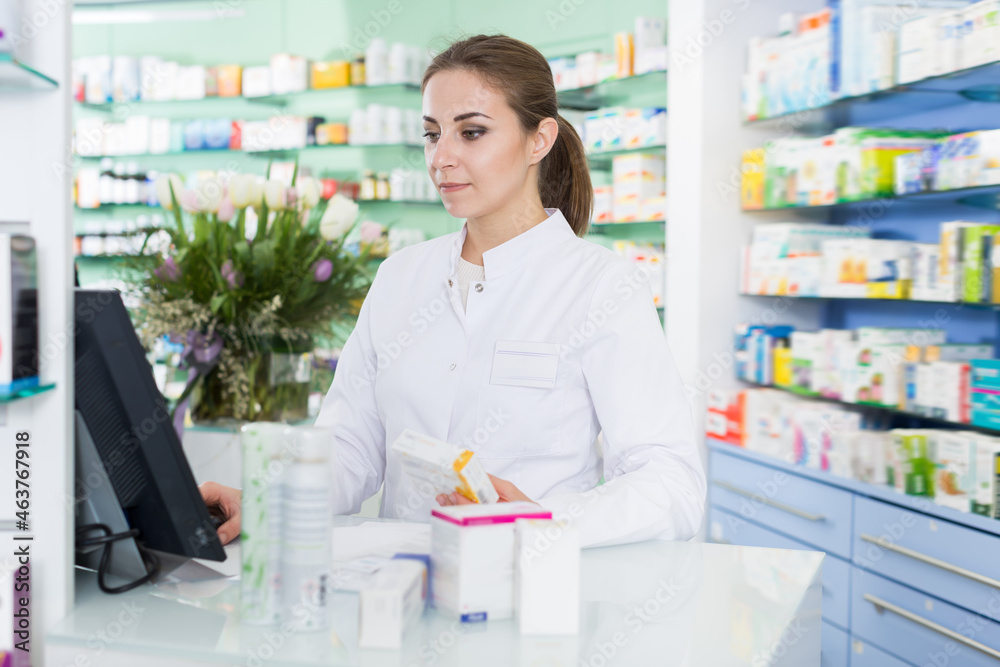 Young woman pharmacist is standing welcoming near cashbox in pharmacy
