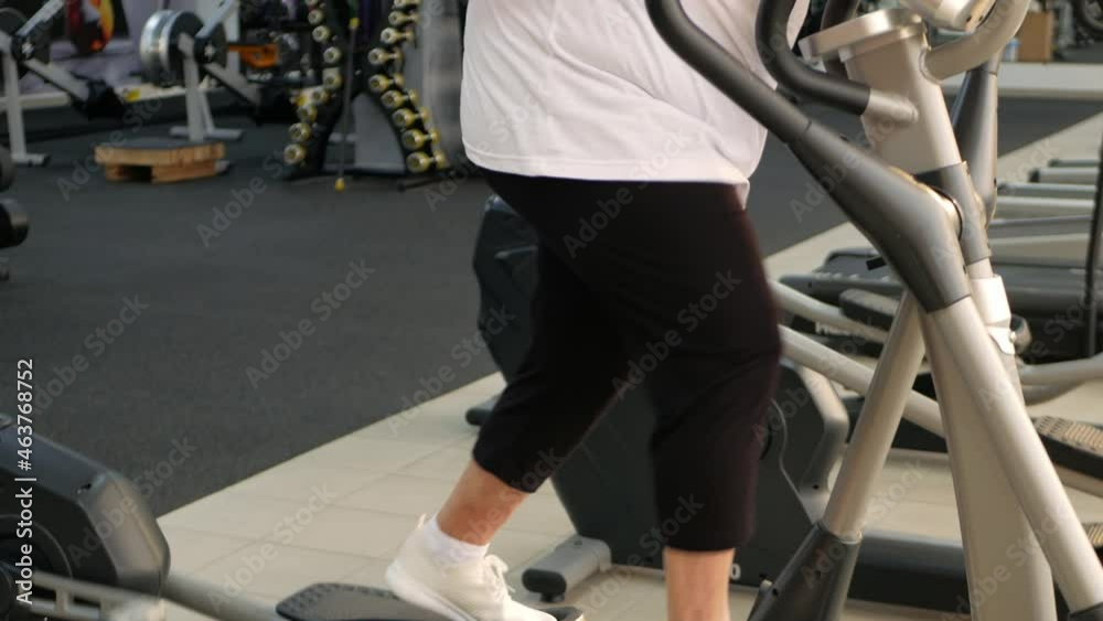 elderly retired woman with gray hair is engaged in sports on simulators in gym. Healthy lifestyle, senior concept, indoor. Rehabilitation, treatment after injuries, improvement. Individual Smiling elderly retired woman with gray hair is engaged in sports on simulators in gym. Healthy lifestyle, senior concept, indoor. Rehabilitation, treatment after injuries, improvement. Individual Smiling