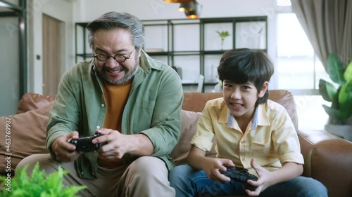 happiness cheerful asian dad son play video game together at
 home fun and excited hand hold joystick in quarantinem oment entertainment at home concept.Smiling family sitting on the couch together photo