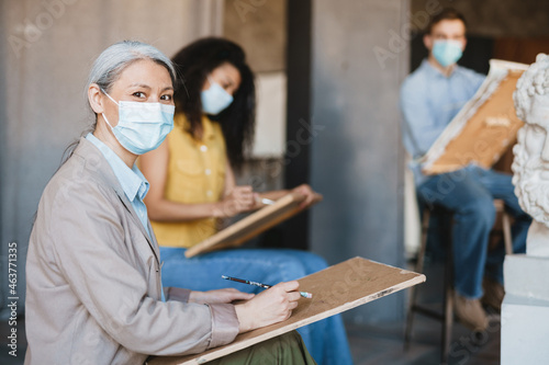 Mature teacher drawing with her students during class in art school