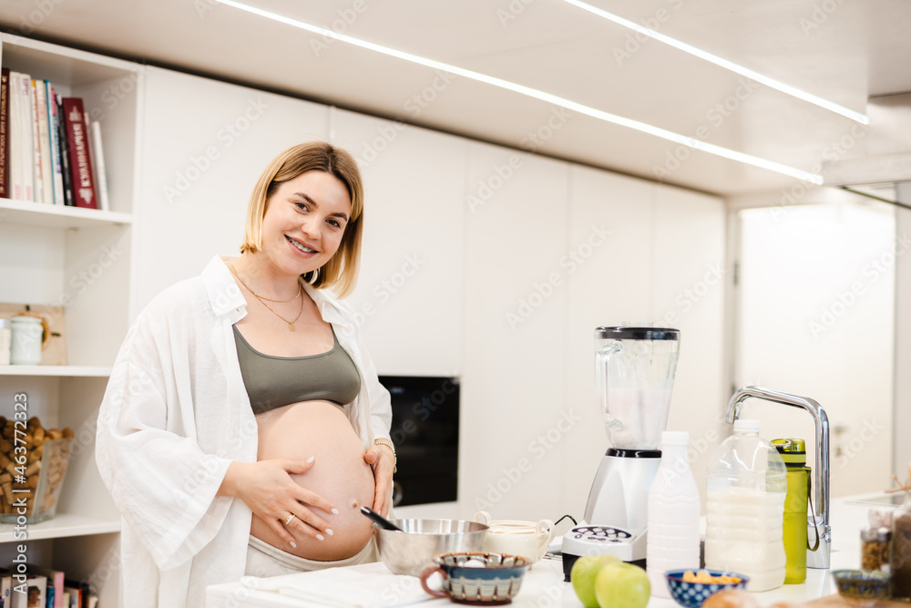 White pregnant woman smiling and touching her belly while cooking White pregnant woman smiling and touching her belly while cooking