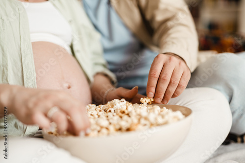 White couple eating popcorn and watching movie while sitting on couch