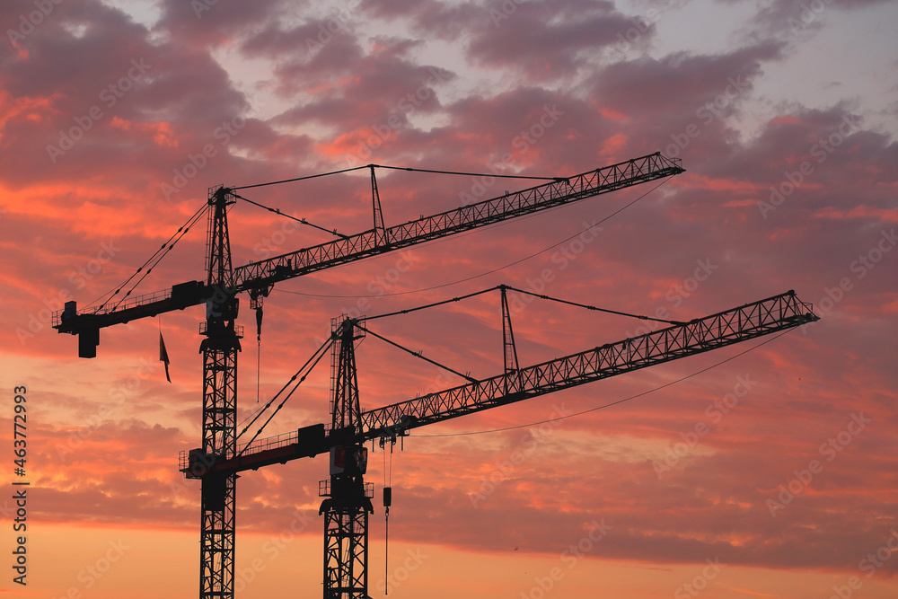 Two large at a construction site against a colorful sky at sunset