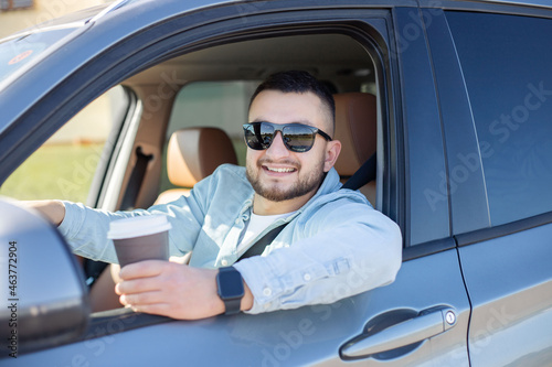 Close up of a smiling man driving a car while drinking coffee. 