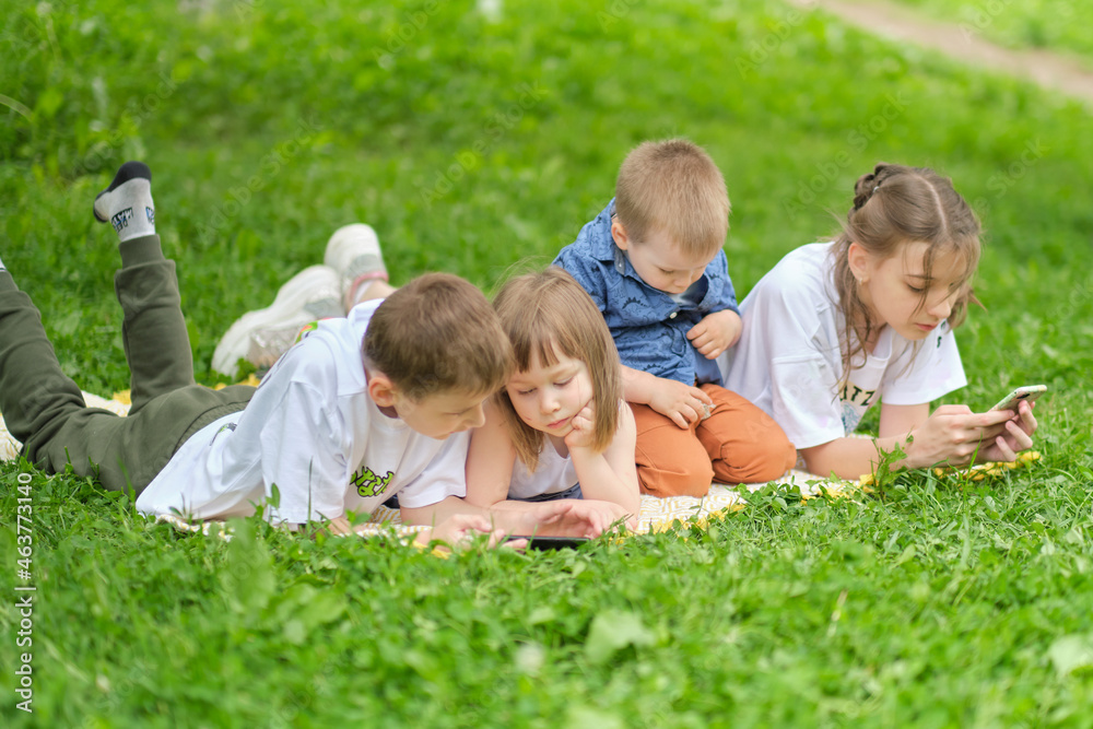 children friend group playing internet with mobile smartphone on grass. Happy children using smartphones sitting on the grass. Brothers and sister. children friend group playing internet with mobile smartphone on grass. Happy children using smartphones sitting on the grass. Brothers and sister.