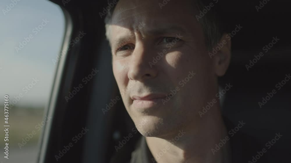 Portrait of a man riding passenger side in a car as he turns to look out the window.