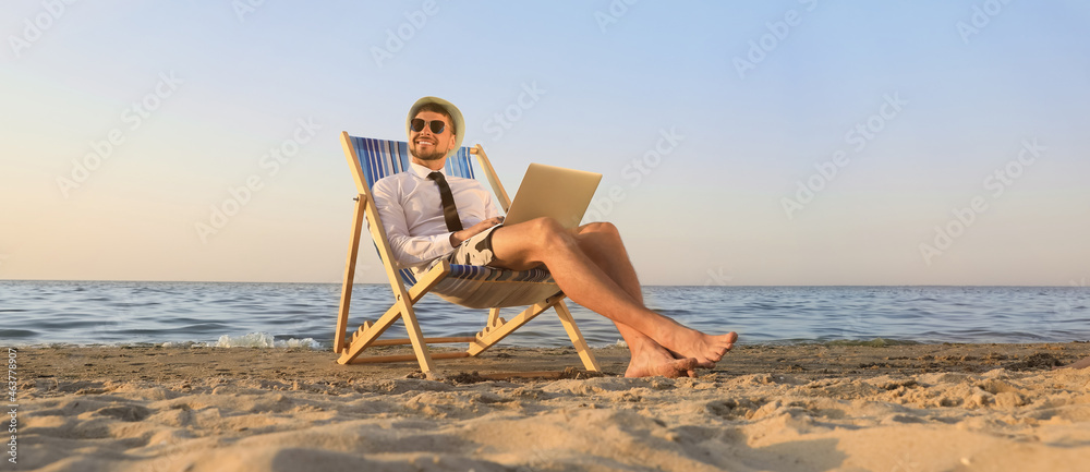 Happy man with laptop resting on deckchair near sea. Business trip - obrazy, fototapety, plakaty 