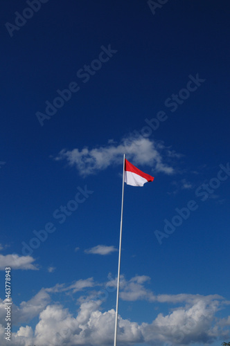 National flag of Indonesia on a flagpole with blue sky background.