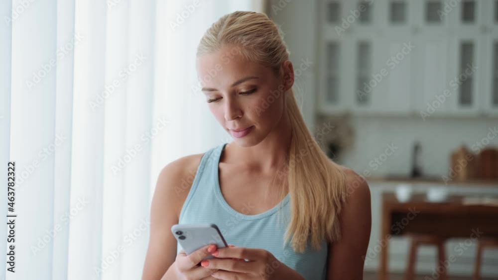 Smiling blond woman texting by phone at home