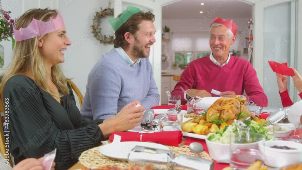 Multi generation family in paper hats reading christmas cracker jokes whilst eating meal together - shot in slow motion Multi generation family in paper hats reading christmas cracker jokes whilst eating meal together - shot in slow motion