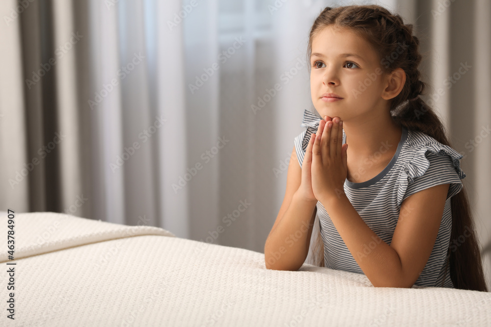 Cute little girl with hands clasped together saying bedtime prayer at home. Space for text