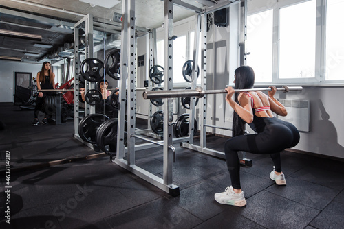 Two women in activewear doing deep squats with barbell