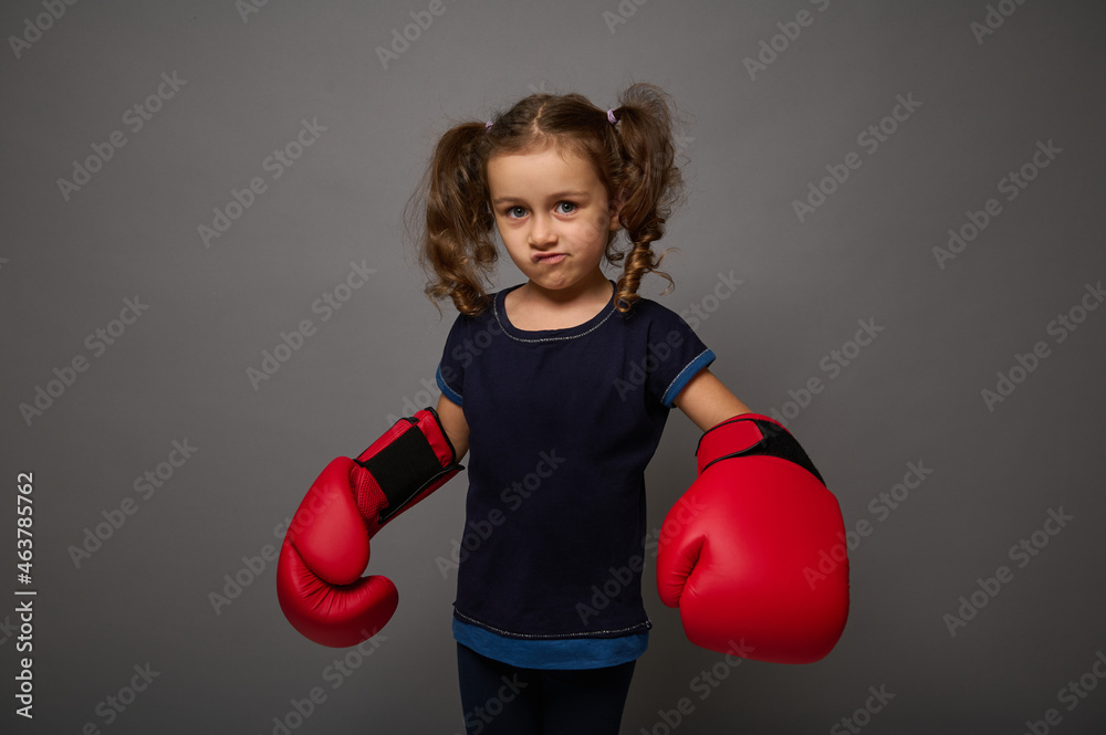 Cute European 4 years old baby girl wearing red boxing gloves poses against gray wall background with copy space for advertisement for Boxing Day Cute European 4 years old baby girl wearing red boxing gloves poses against gray wall background with copy space for advertisement for Boxing Day