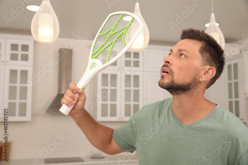 Man with electric fly swatter in kitchen. Insect killer photo