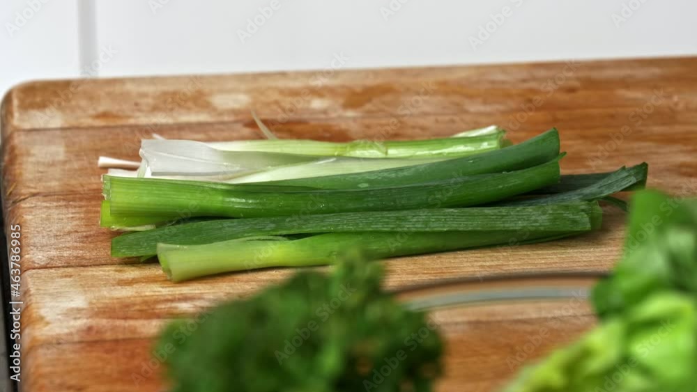 Green onions prepped on a wooden cutting board with a bowl of broccoli in the foreground Green onions prepped on a wooden cutting board with a bowl of broccoli in the foreground