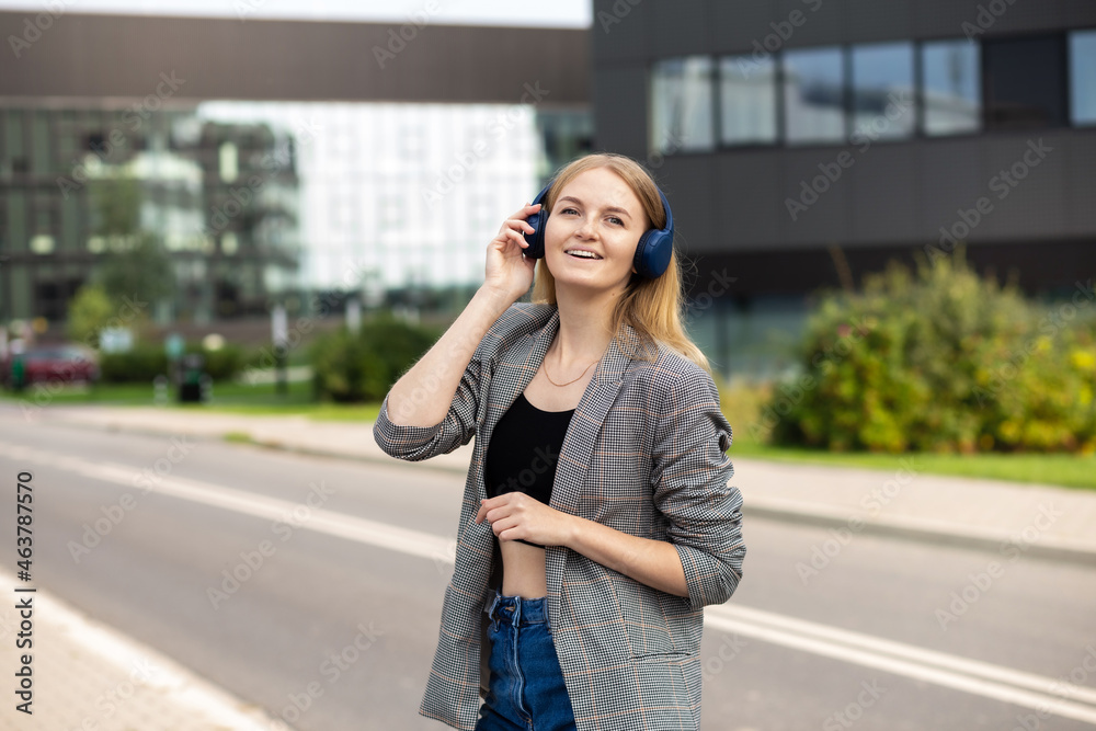 Portrait of young happy woman listening to music with headphones and smiling while walking on the street in the city. Music lover enjoying music. Portrait of businesswoman walking and smiling outdoor