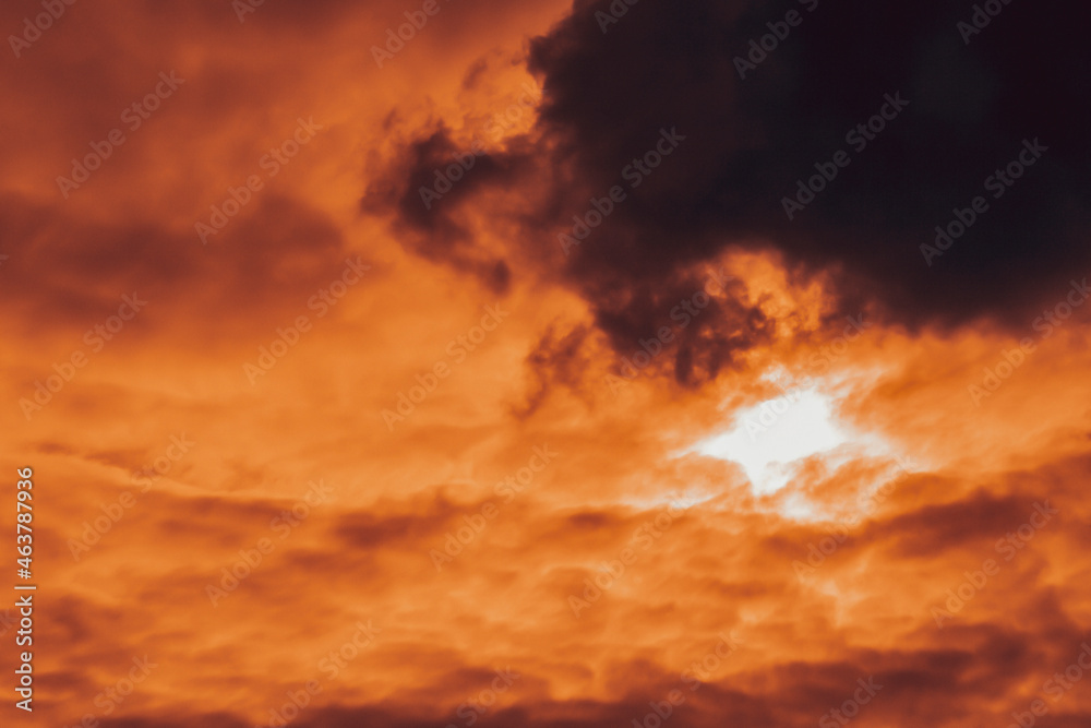 Cloudy landscape in autumn in orange colors with an overhanging rain cloud. The sun rim is slightly visible in the general bright light of the source. Light morning haze, twilight.  Selective focus.