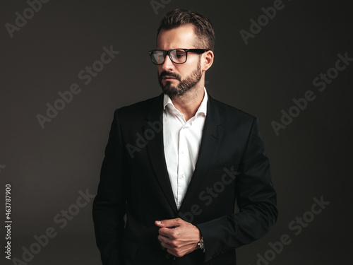 Portrait of handsome confident stylish hipster lambersexual model. Sexy modern man dressed in elegant black suit. Fashion male posing in studio on dark background. In spectacles