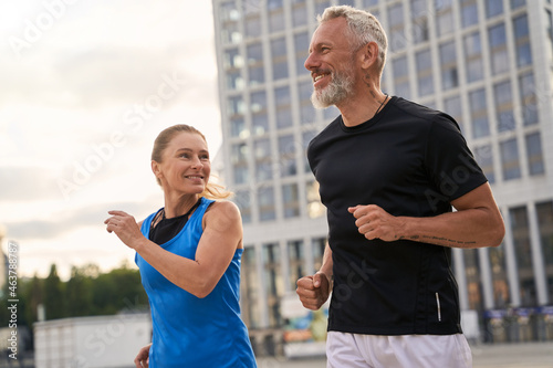 Portrait of active middle aged couple, man and woman in sportswear looking happy while jogging together outdoors, having mroning workout