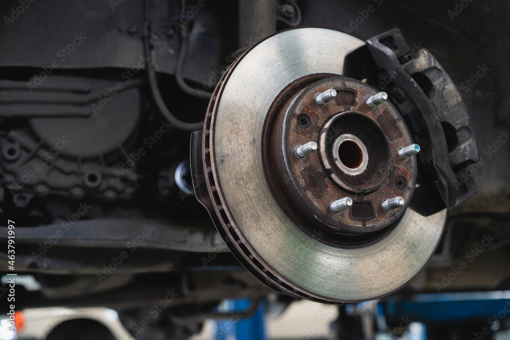 Old caliper break and disc break in a vehicle, an old car lifted up on the hydraulic ramp for inspection and maintenance in garage.