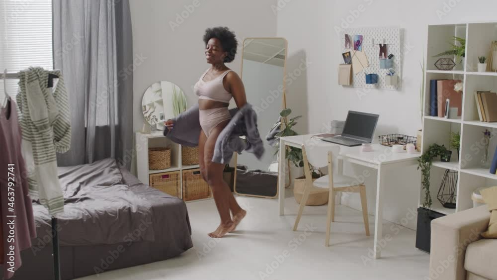 Full-length slowmo shot of young confident plus size African-American woman in casual pink underwear dancing at bedroom alone spending time with herself Full-length slowmo shot of young confident plus size African-American woman in casual pink underwear dancing at bedroom alone spending time with herself