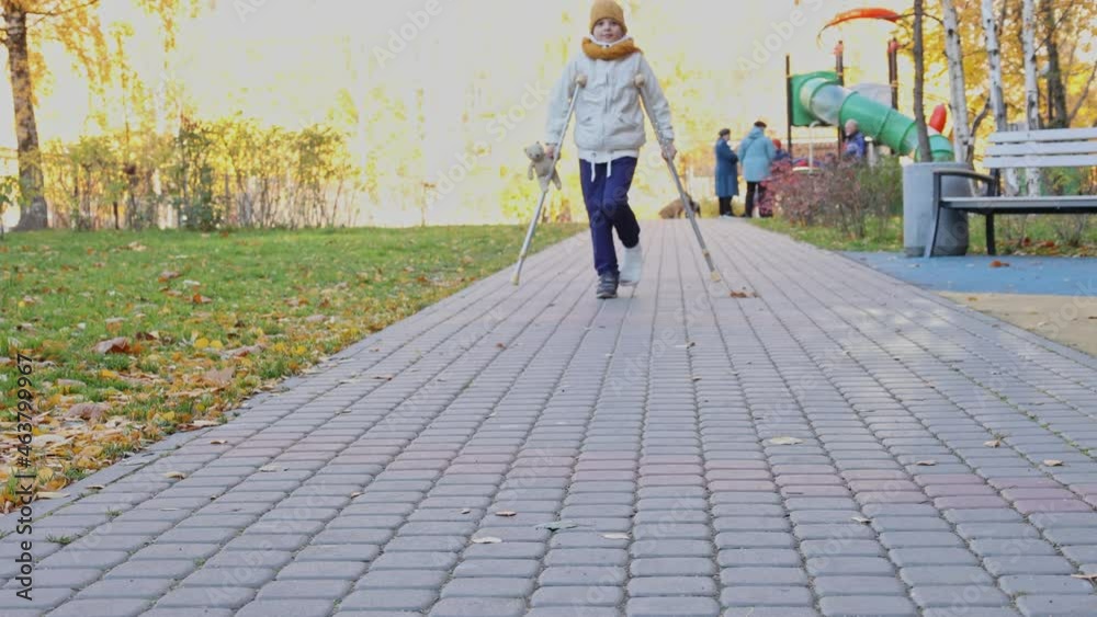 Kid walks in autumn park on crutches. Girl has one leg broken in cast. Kid walks in autumn park on crutches. Girl has one leg broken in cast.